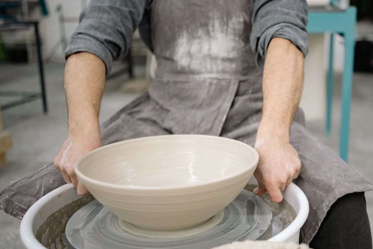 Services-02 Close-up of hands shaping a ceramic bowl on a potter's wheel in a workshop.
